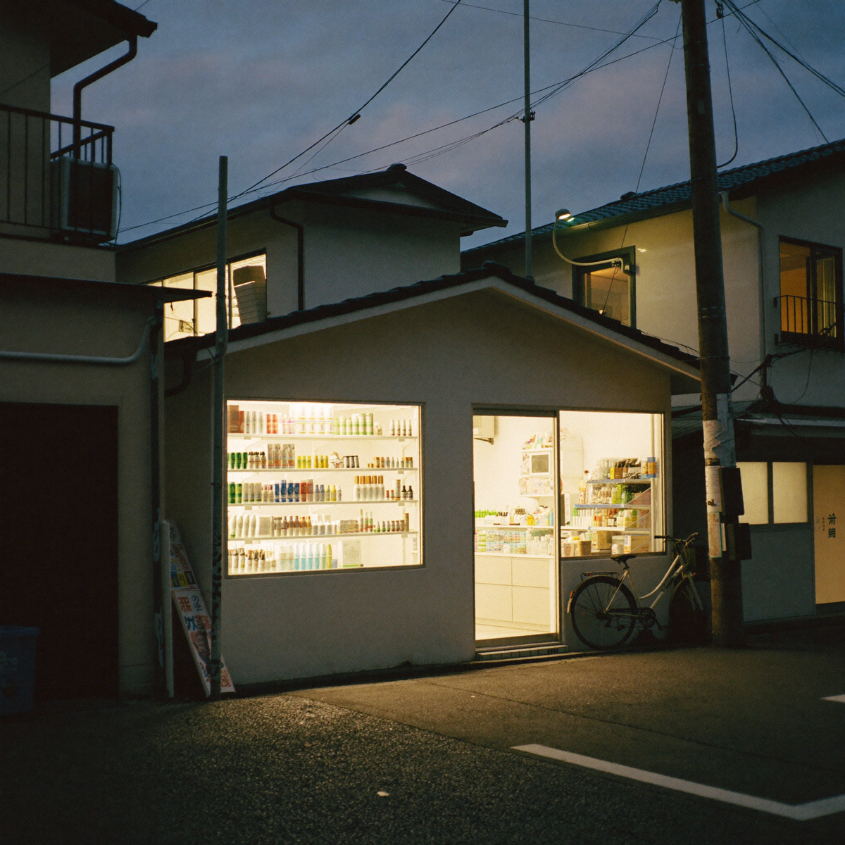 A Japanese street at dusk with a convenience store glowing