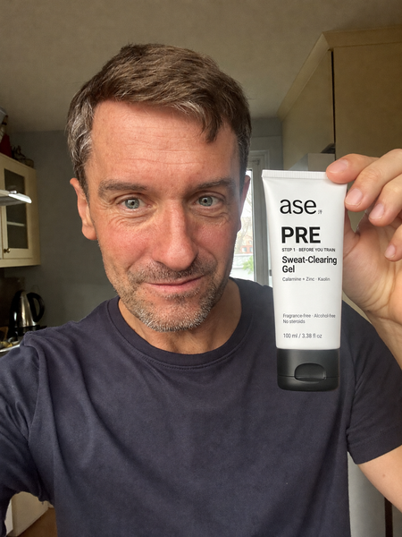 A man holding an ASE PRE Sweat-Clearing Gel tube in his kitchen.